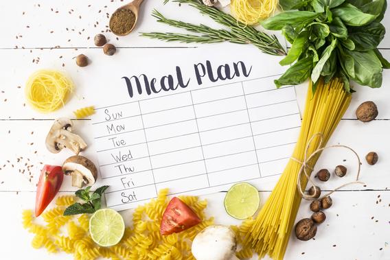 Dry pasta, herbs and spices arranged around a meal plan template