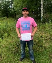 Cory Babbs stands in the woods holding a sign that says "influencer". 